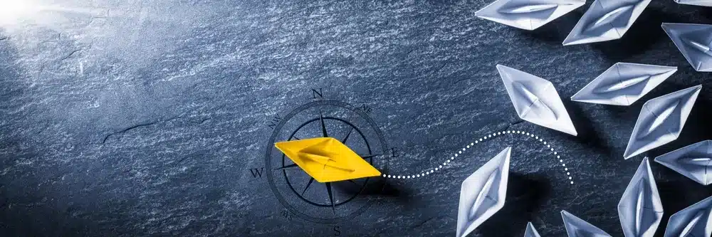 a paper boat navigating away from a group of paper boats