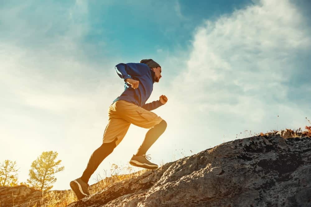 Skyrunner athlete embraces outdoor activities for addiction recovery and nature immersion running uphill against a sunset