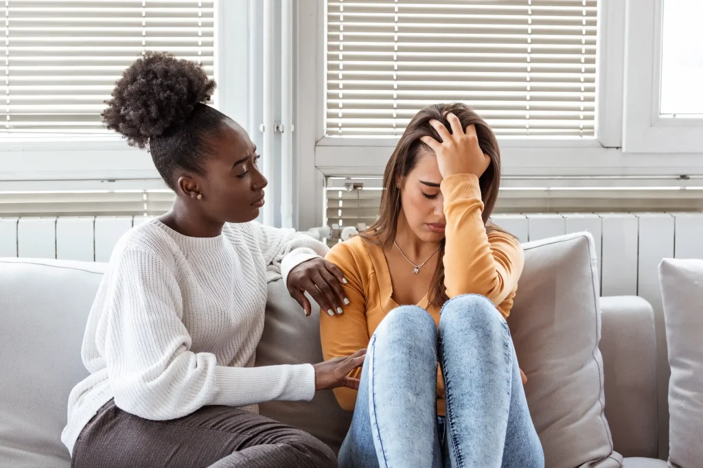 Young woman looking unwell and holding her head while a friend checks on her, representing the early signs of alcohol poisoning or heatstroke during Spring Break.